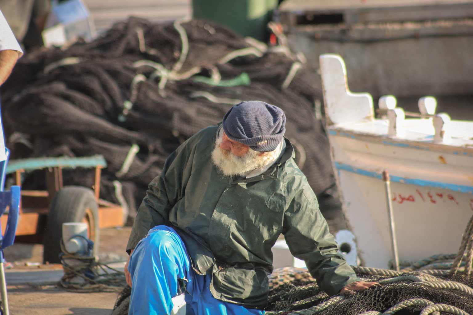 A fisherman in a cap sorting his nets beside the boats