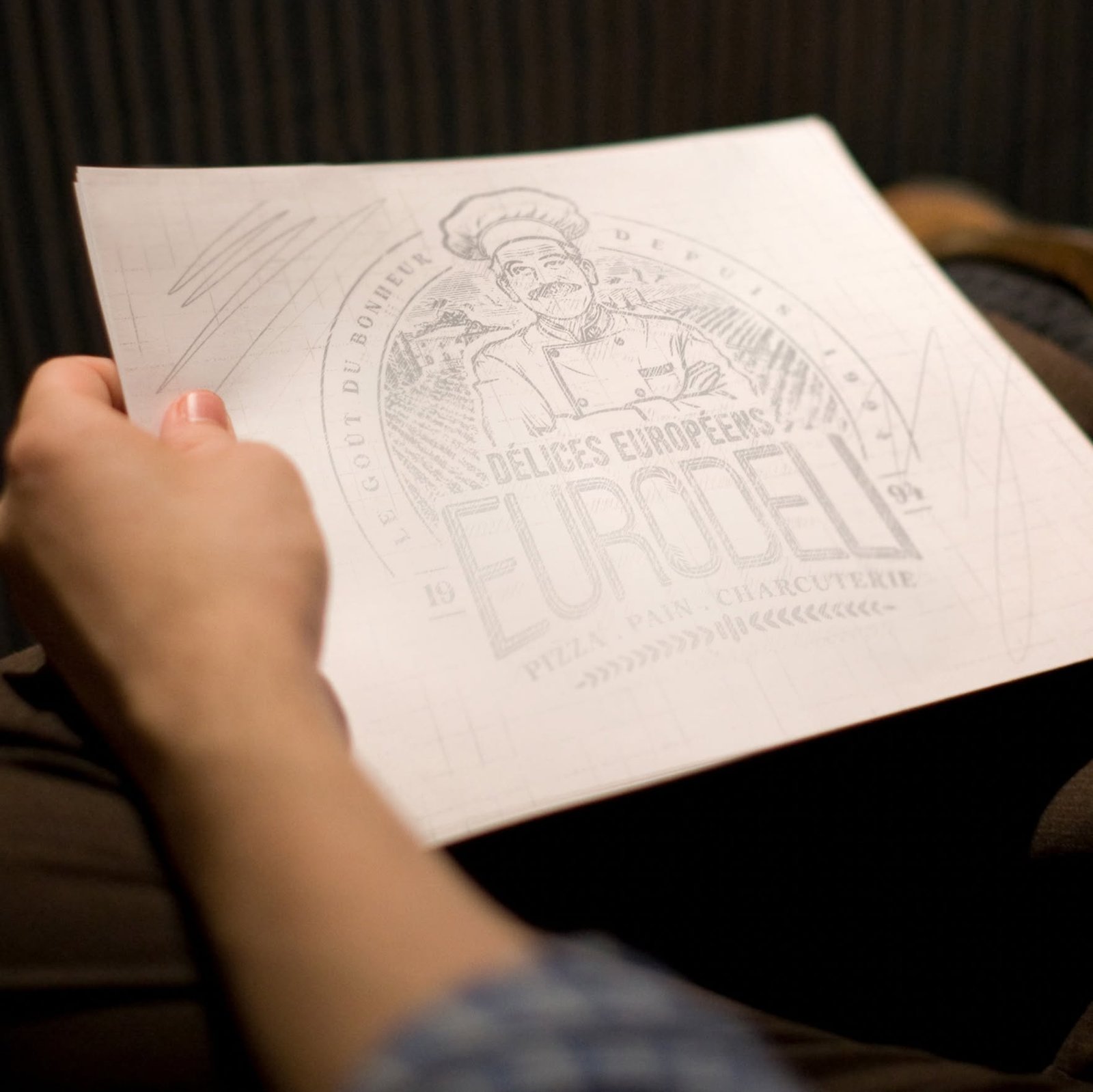 A photo showing the detailed hand-drawn sketch of the Euro Deli logo being held.