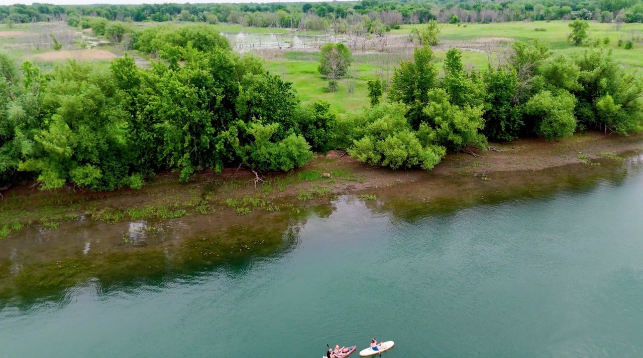 A person kayaking on a calm river, seen from above.